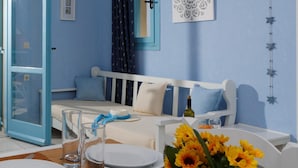 A room with a blue wall, a white bed with blue curtains, a white table set for dining, and a wall decoration. - Piskopiano Village (Hersonissos)