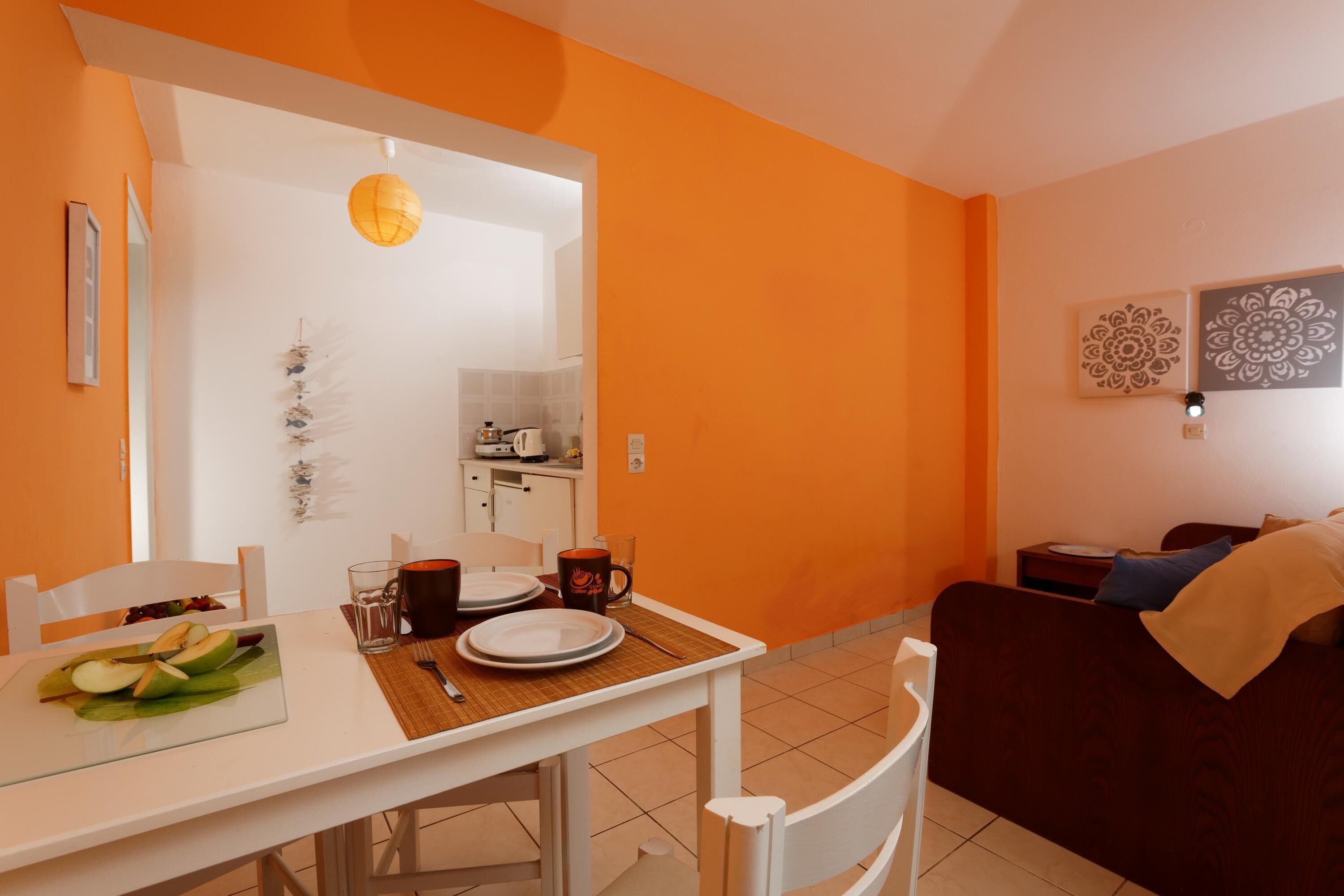 A dining area with a white table, orange walls, and a kitchen in the background.