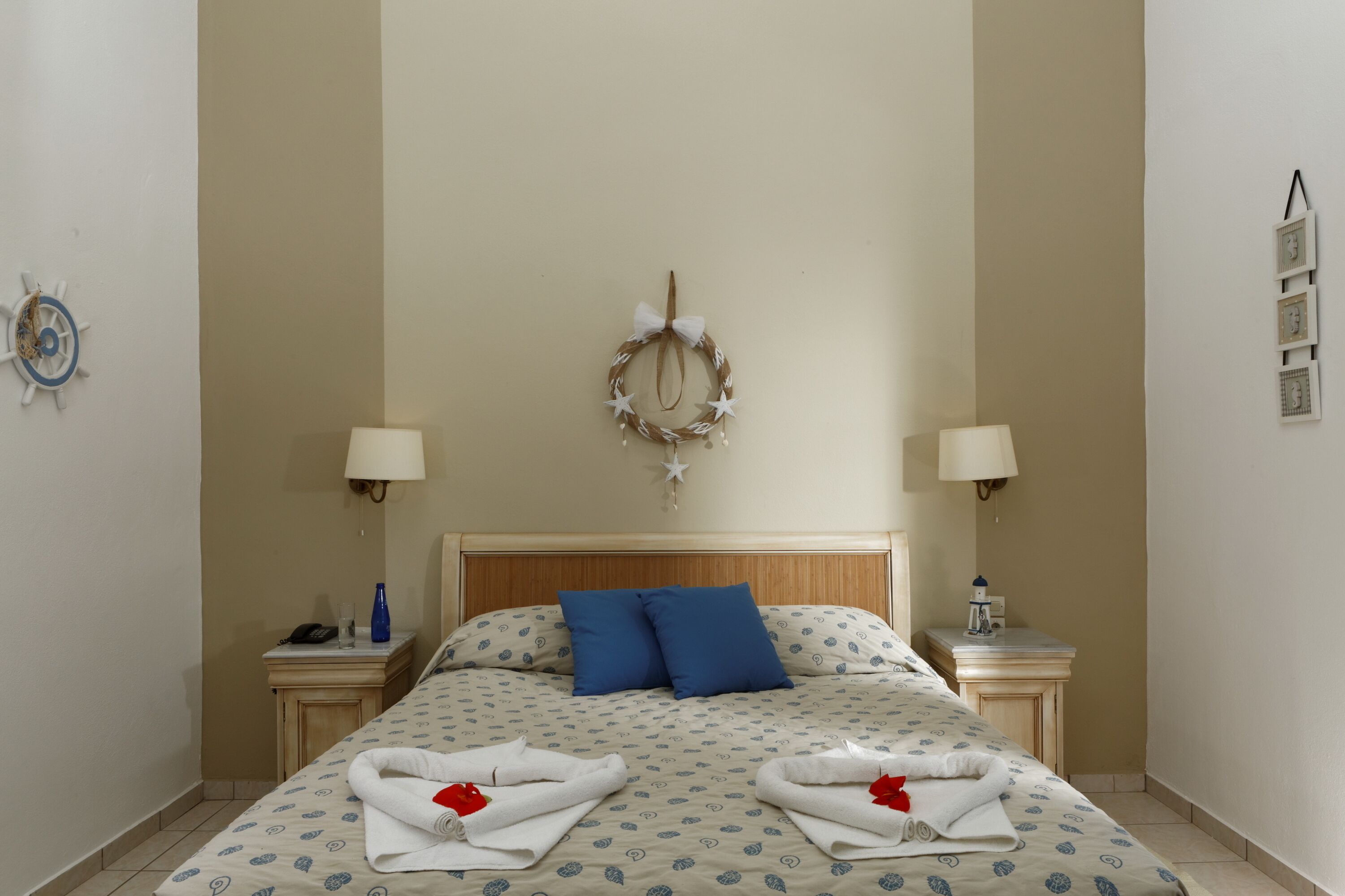 Una cama bien hecha con una colcha estampada, dos almohadas azules y una guirnalda decorativa en la cabecera.
