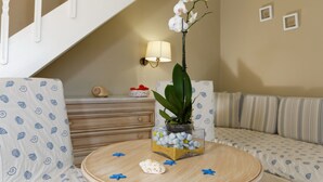A living room with a sofa, a coffee table with decorative items, a staircase, and a wall-mounted lamp. - Piskopiano Village (Hersonissos)