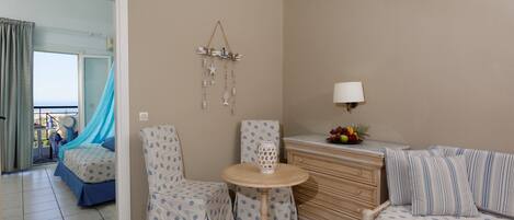 A room with a bed, a chair, a table, a lamp, and a dresser.