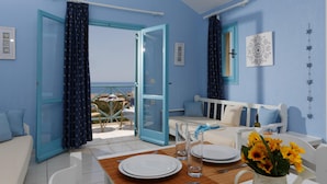A room with a balcony, a dining table set with plates and glasses, a sofa, and a view of the sea. - Piskopiano Village (Hersonissos)
