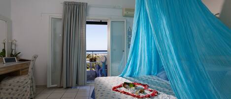 Camera da letto con un letto ricoperto da un baldacchino blu, una scrivania con un portatile e vista sull'esterno attraverso una porta.