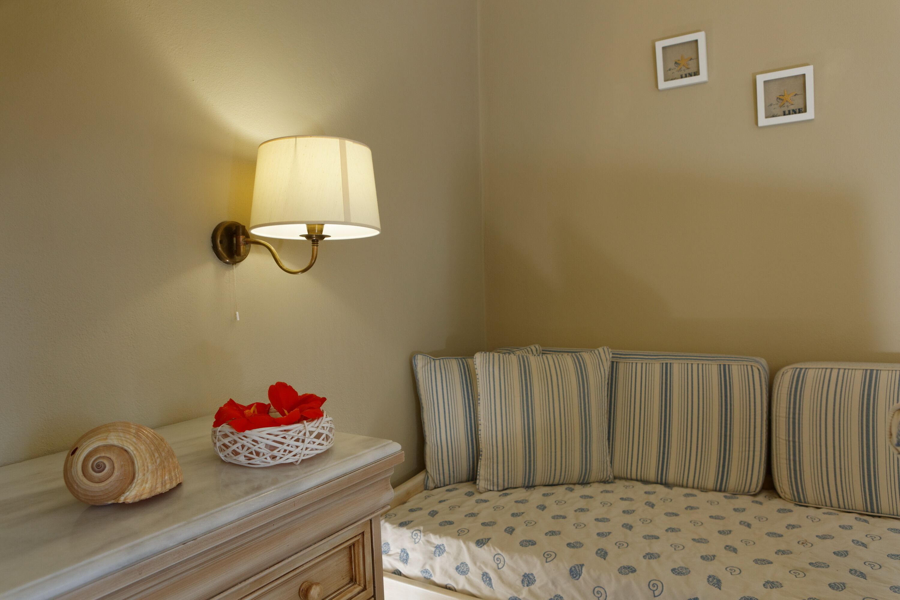 A bedroom with a bed, a bedside table with a lamp, a decorative shell, and a basket of red flowers.