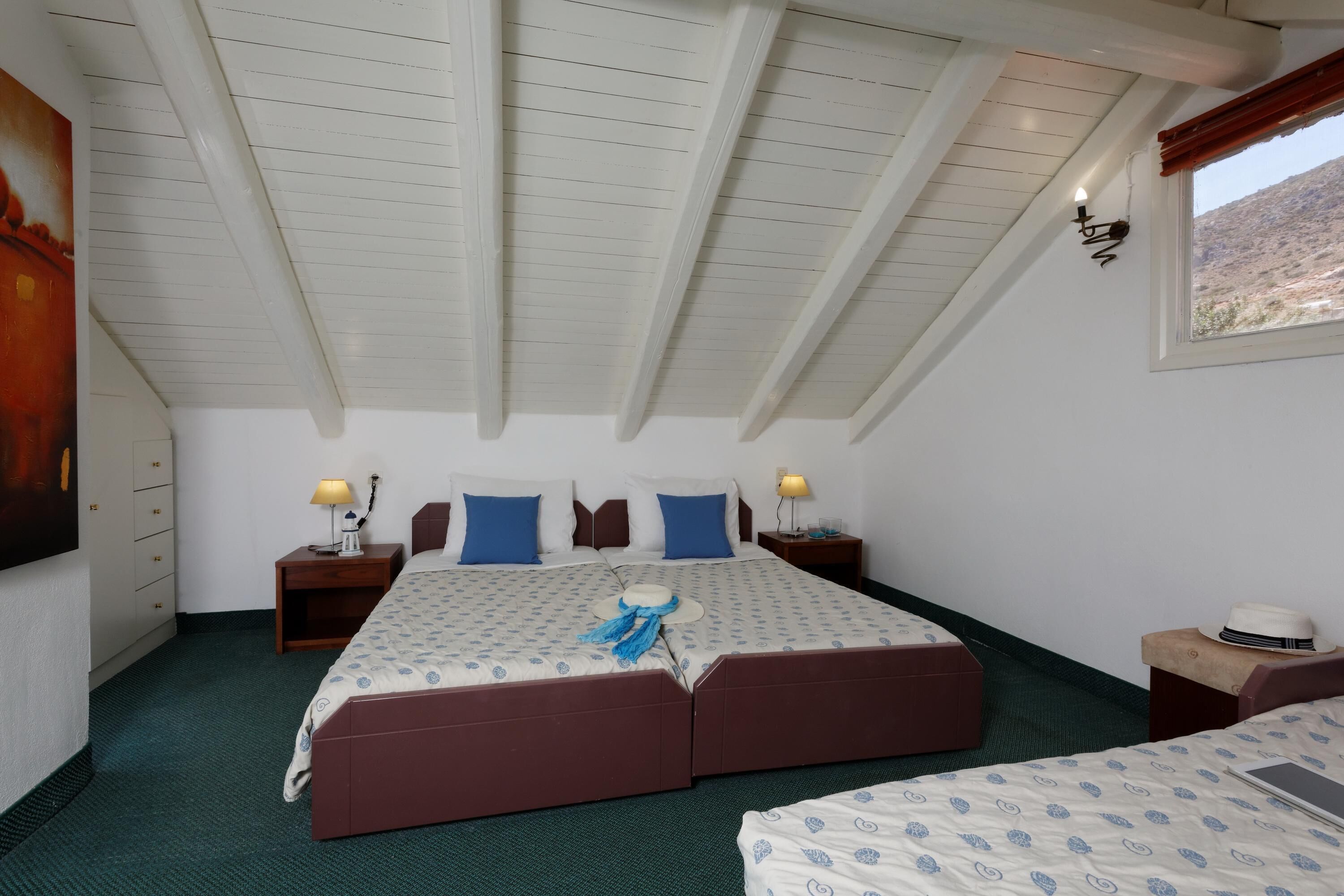 Un lit double avec une couvre-lit à motifs, deux lampes de chevet, une table de chevet, un chapeau et un tableau accroché au mur.