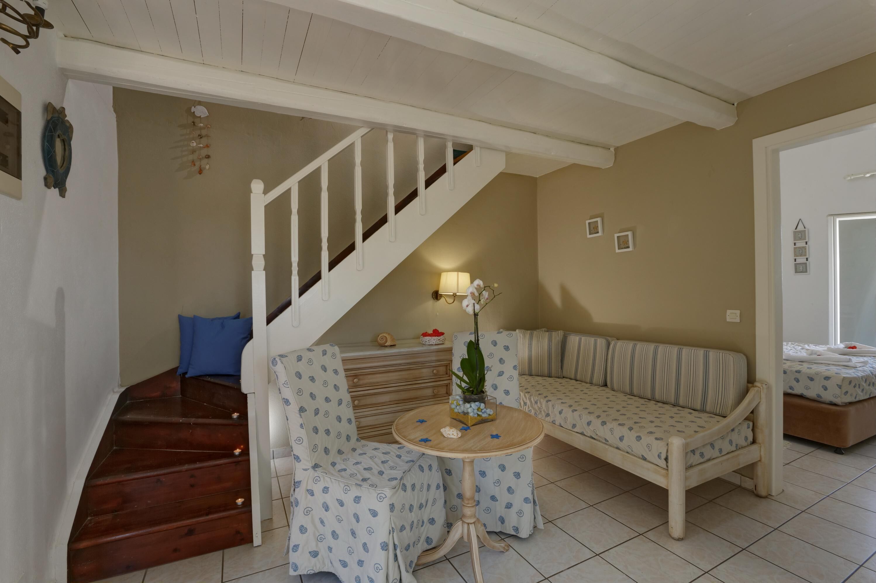 A cozy living room with a wooden staircase, a striped sofa, a small round table with a plant, and a blue pillow on the floor.
