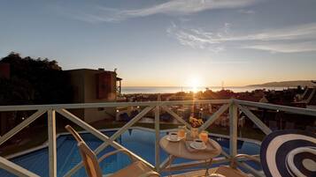 A poolside view with a table set for two, overlooking a cityscape at sunset.