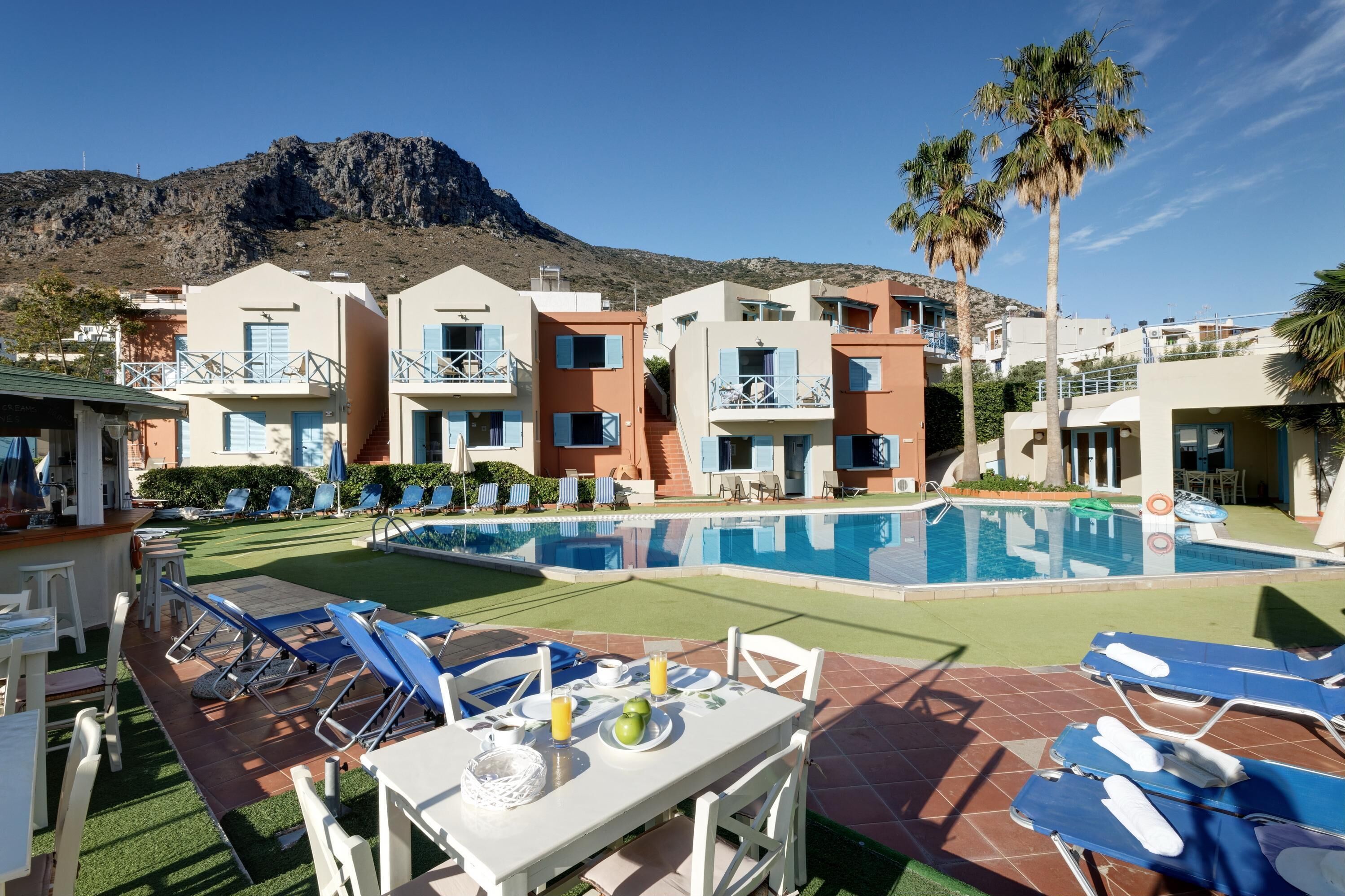 A poolside area with lounge chairs, a dining table, and a mountain backdrop.