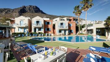 A poolside area with lounge chairs, a dining table, and a mountain backdrop.