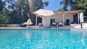 A swimming pool with a covered seating area, surrounded by trees and a white building. - Luxurious Villa Anna Maria (Kassandra)