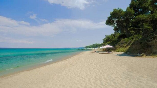 A beach with clear turquoise water, a sandy shore, and a small structure with a roof. - Luxurious Villa Anna Maria (Kassandra)