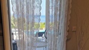 A room with a sliding glass door featuring white lace curtains, a tiled floor, and a view of an outdoor seating area with a table and chairs. - Luxurious Villa Anna Maria (Kassandra)