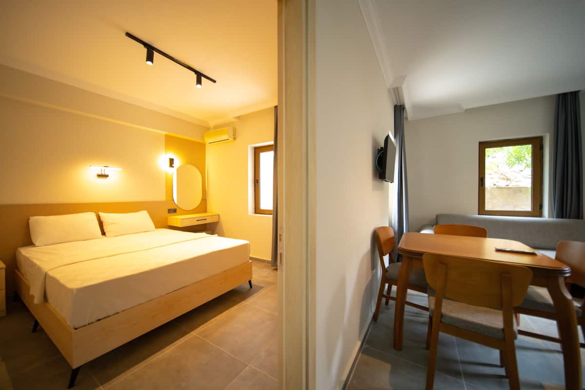 A hotel room with a bed, bedside table, lamp, and a view of the outside.