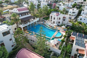 Un quartier résidentiel doté d’une piscine, entouré de bâtiments blancs, de palmiers et d’une construction au toit rouge.