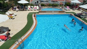 Une piscine avec une terrasse carrelée, des chaises longues et des parasols.