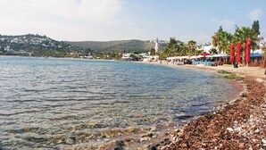 Una playa con agua cristalina, costera de guijarros y un pueblo al fondo.