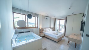 Un dormitorio moderno con una cama grande, un baño independiente con bañera y vistas a la ciudad a través de amplios ventanales.