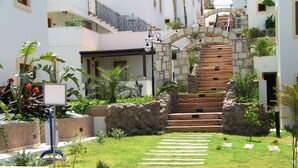 Un patio con una escalera de piedra que lleva al segundo piso, rodeado de follaje y un muro de piedra.