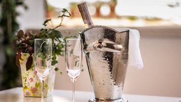 A metallic ice bucket with a bottle of champagne, a glass, and a floral vase on a table.