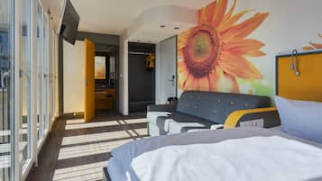 Habitación de hotel moderna con una cama grande, un sofá, una pared con un mural de girasoles y vistas a través de la puerta de vidrio.