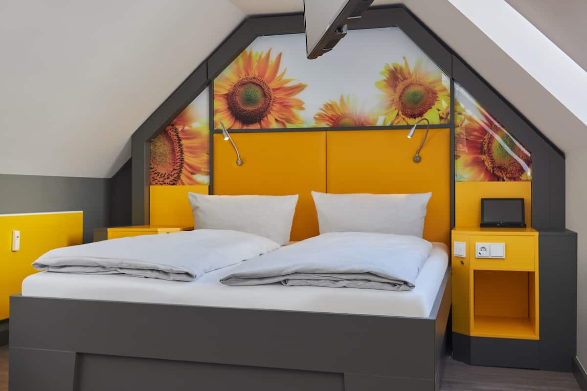 Une chambre moderne avec un lit, deux tables de chevet et un mur recouvert d’un papier peint à motifs de tournesols.