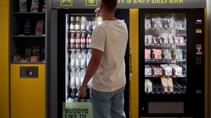 A vending machine with a sign that reads "Buddy's 24/7 deli bar" and a sign below it stating "Buddy's like to drink." - Buddy Hotel (Munich)