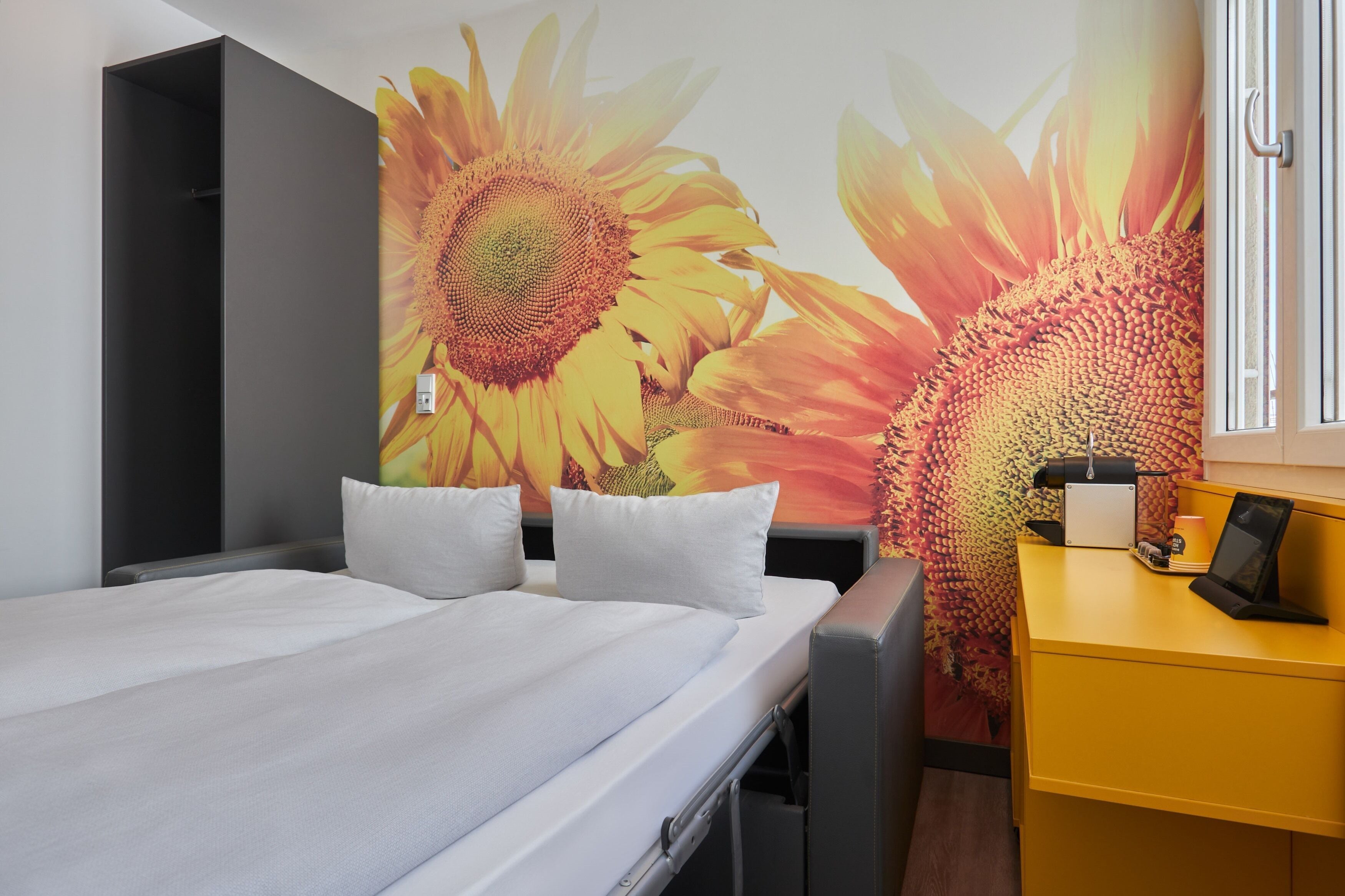 Une chambre avec un lit, un bureau et une fresque murale représentant des tournesols.