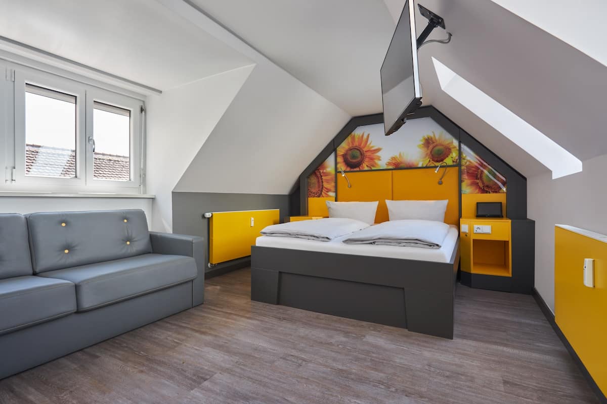 Une chambre à coucher avec un lit, un canapé gris et une fenêtre.