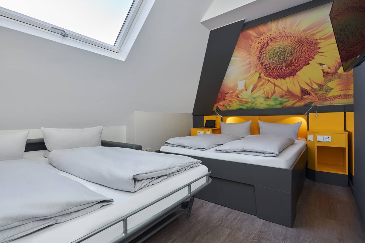 Une chambre d’hôtel moderne avec deux lits, une grande fenêtre et une fresque représentant des tournesols.