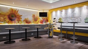 A modern lounge area with a sofa, round tables, a snack cart, and a wall map. - Buddy Hotel (Munich)