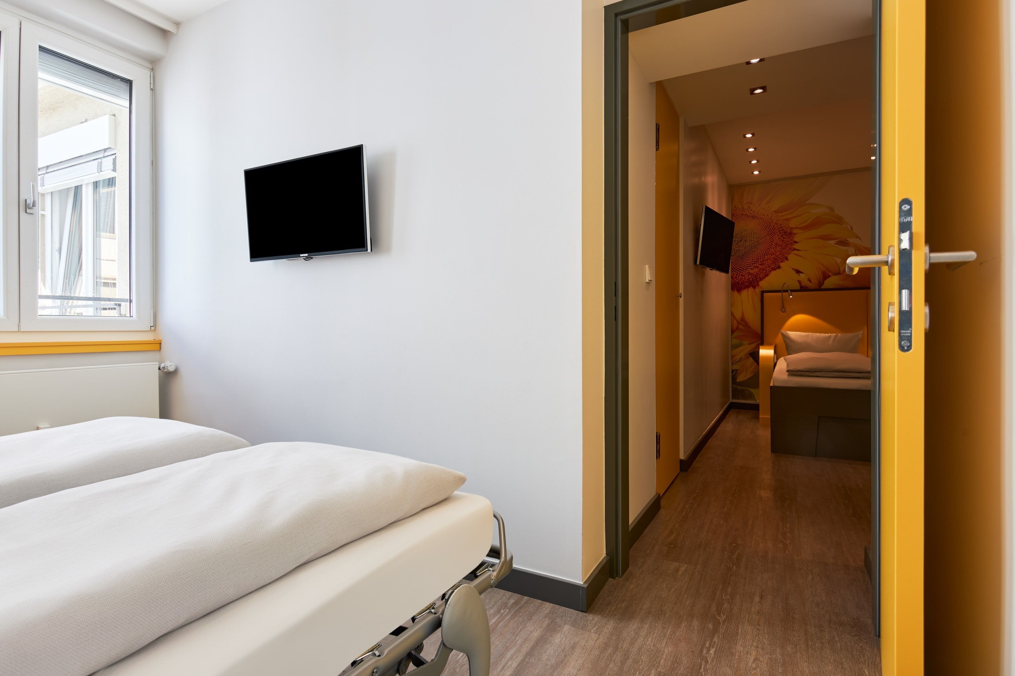 A hotel room with a bed, a flat-screen TV mounted on the wall, and a door leading to a bathroom with a towel and a mirror.