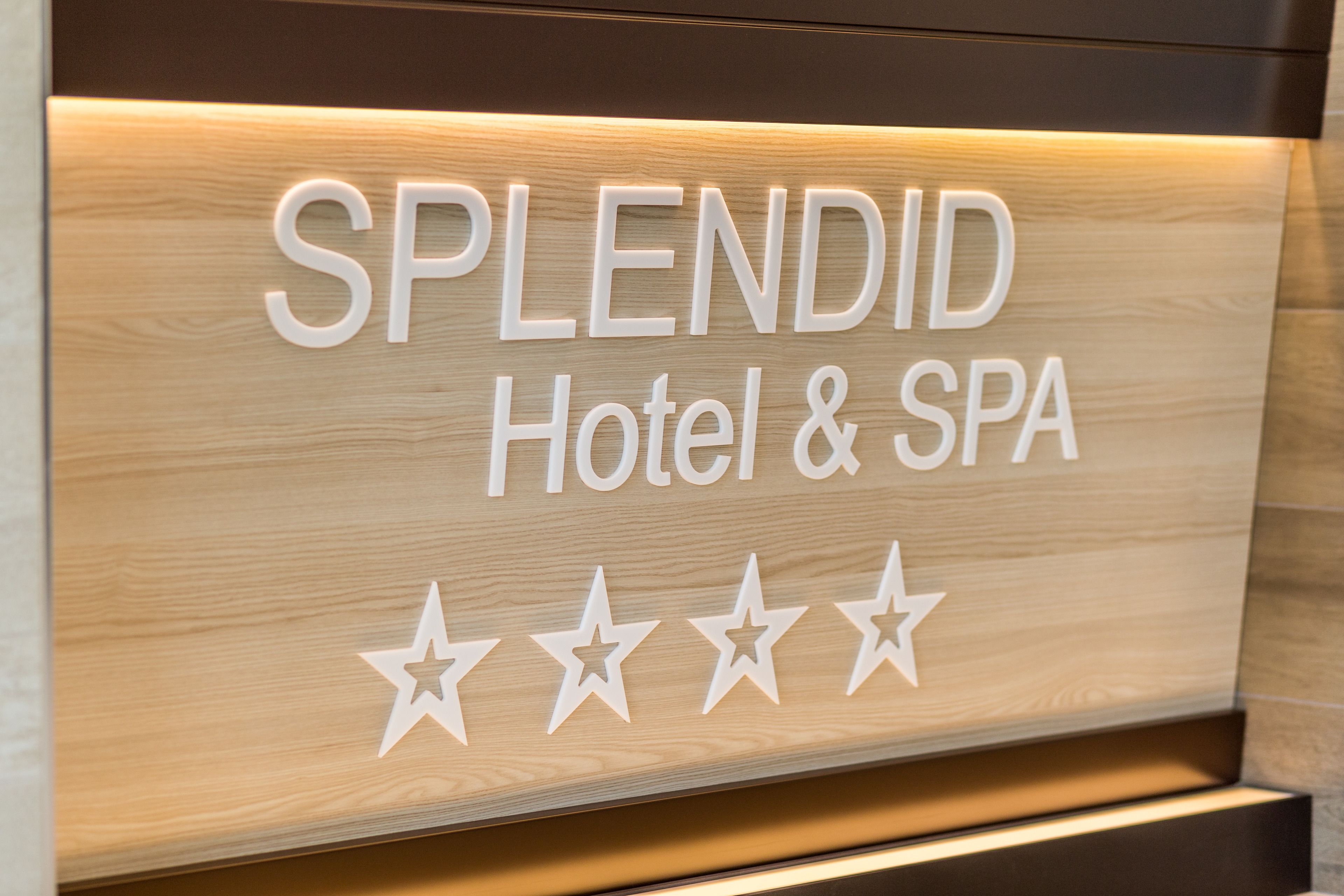 Een bord voor Splendid Hotel & Spa, met een houten achtergrond en vier sterren.