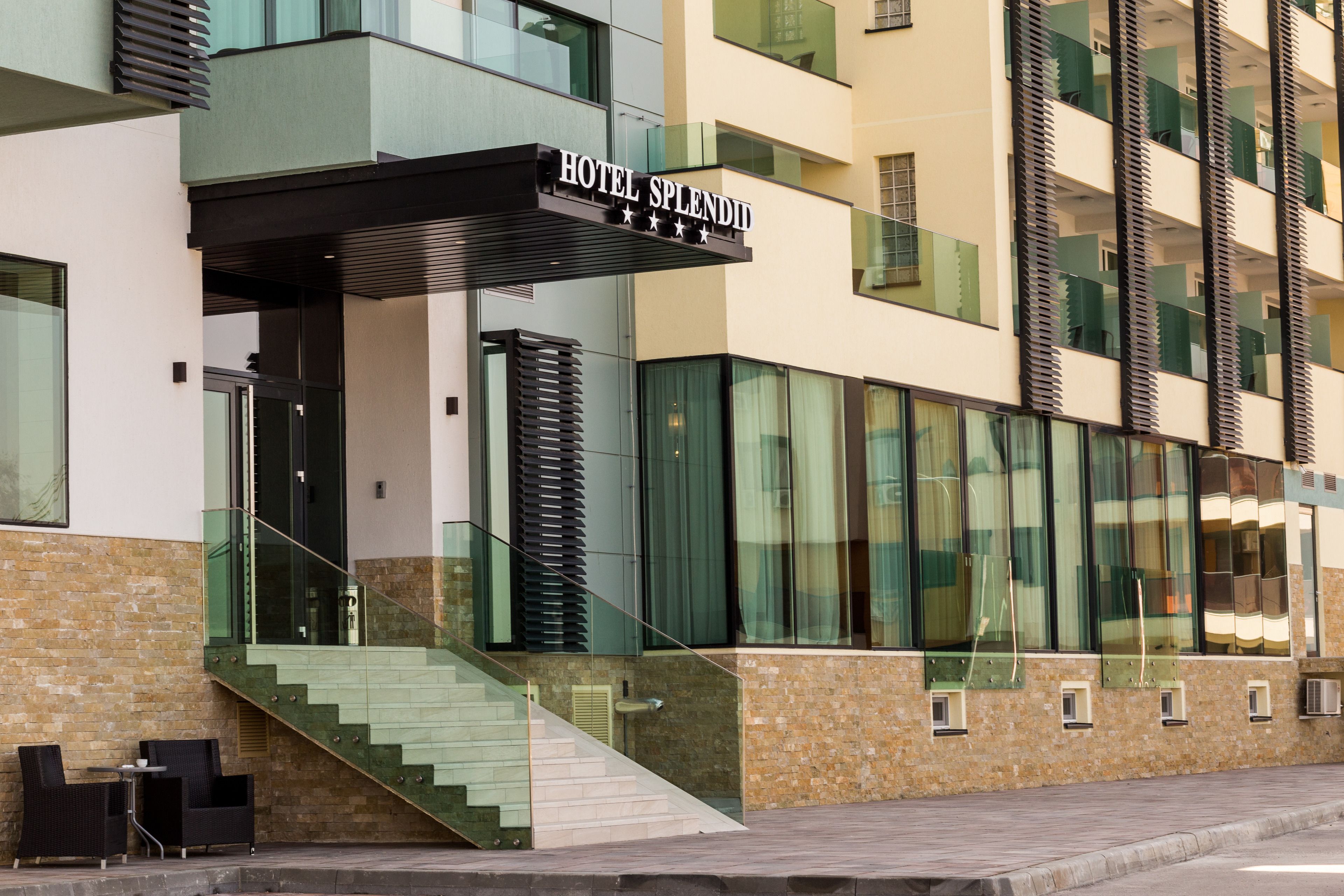 Un hotel moderno con un letrero llamativo que dice "HOTEL SPLENDIT". Cuenta con fachada de vidrio, una escalera que conduce a la entrada y una fachada de ladrillo.