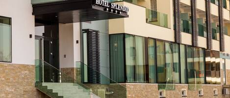 Un hotel moderno con un letrero llamativo que dice "HOTEL SPLENDIT". Cuenta con fachada de vidrio, una escalera que conduce a la entrada y una fachada de ladrillo.