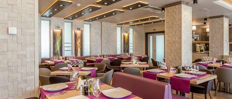 Un interior de restaurante moderno con varias mesas, cabinas acolchadas y lámparas de diseño contemporáneo.