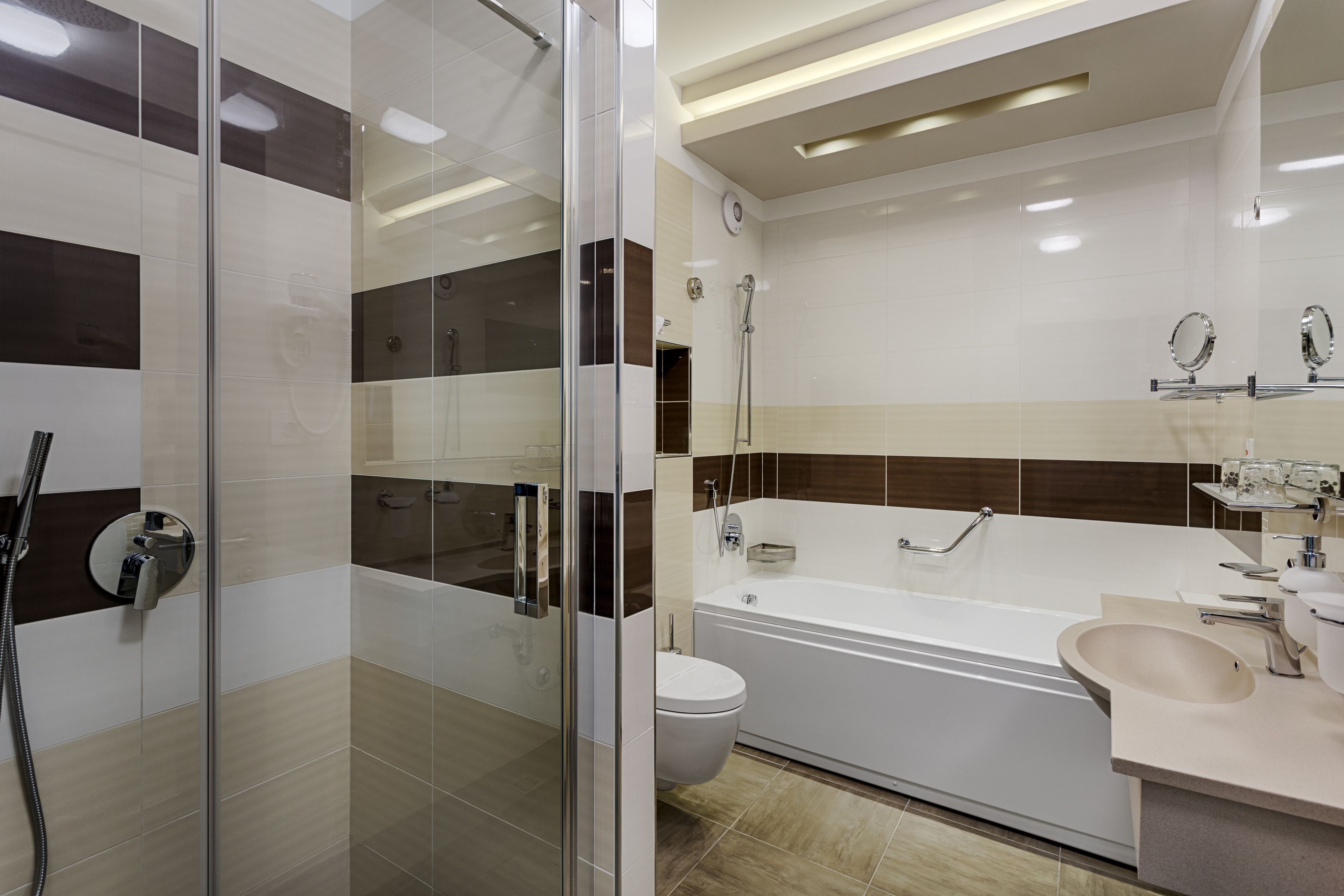 Un baño moderno con ducha de vidrio, una bañera blanca, inodoro y lavamanos con espejo.