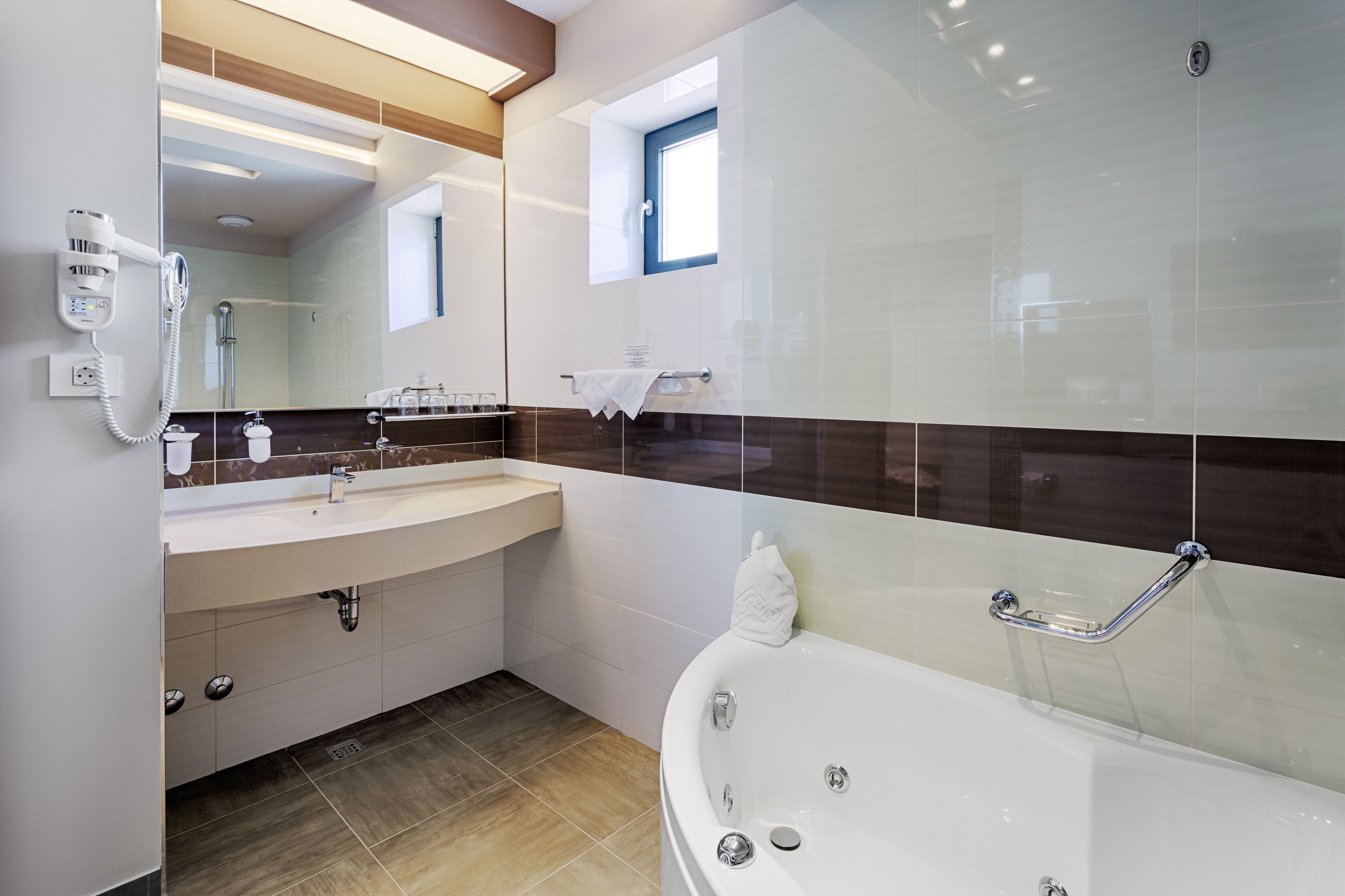 Ein modernes Badezimmer mit einem großen Spiegel, einem Waschtisch mit Waschbecken, einer Badewanne mit Duschbrause und einem Fenster für natürliches Licht.