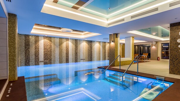 A modern indoor swimming pool with clear water, a glass ceiling, and a tiled wall with a mosaic pattern. - New Splendid Hotel & Spa - Adults Only (Constanta)