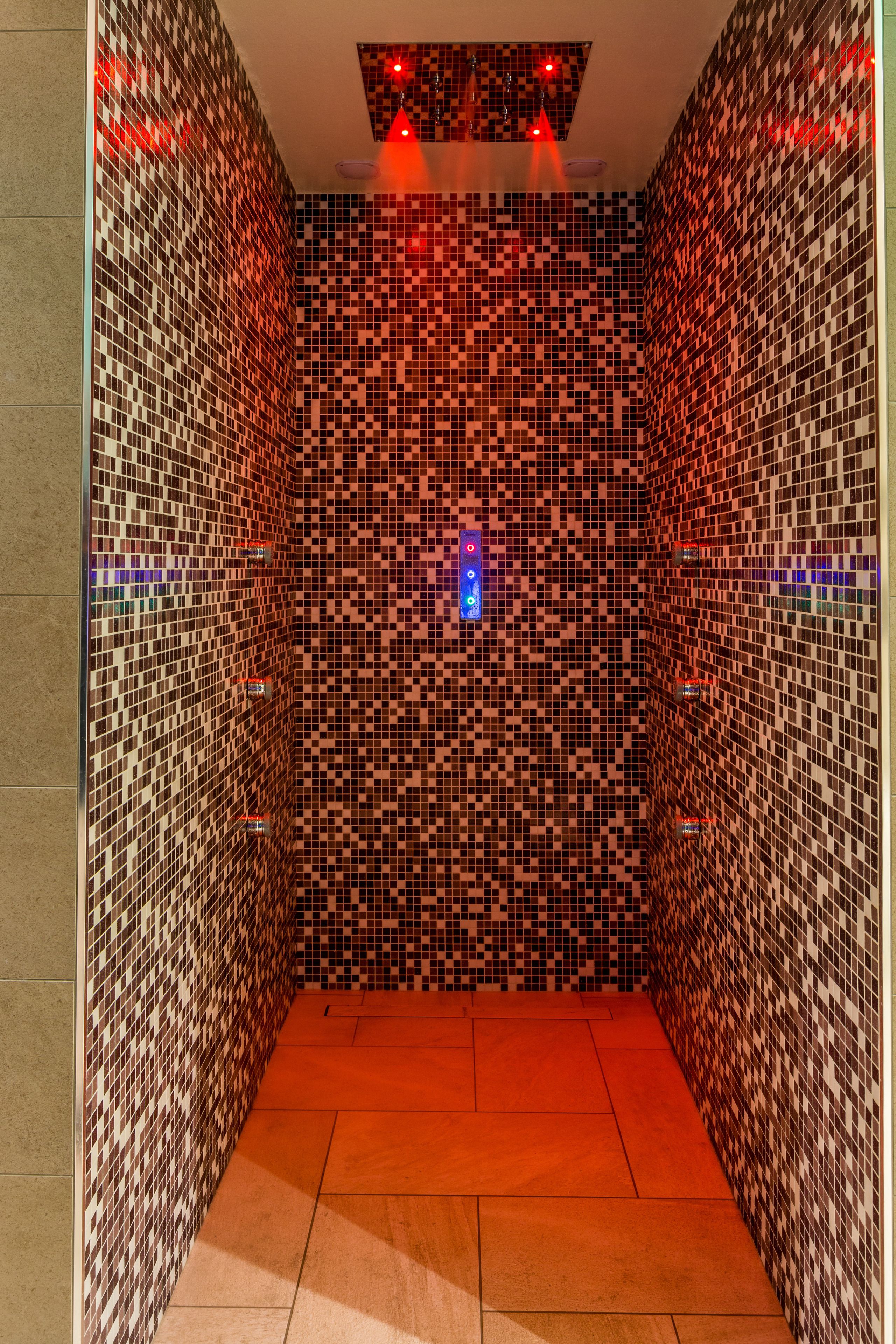 A tiled shower with a checkered pattern and a blue light fixture.