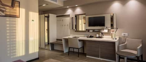 A modern hotel room with a kitchenette, a large mirror, a flat-screen TV, and a seating area with a round table and two chairs.