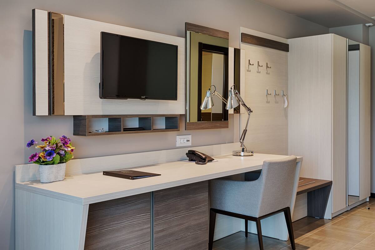 A modern hotel room with a large flat-screen TV, a desk with a telephone, and a chair.