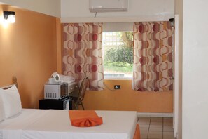 A hotel room with a bed, a desk with a computer, a chair, and a window with curtains.