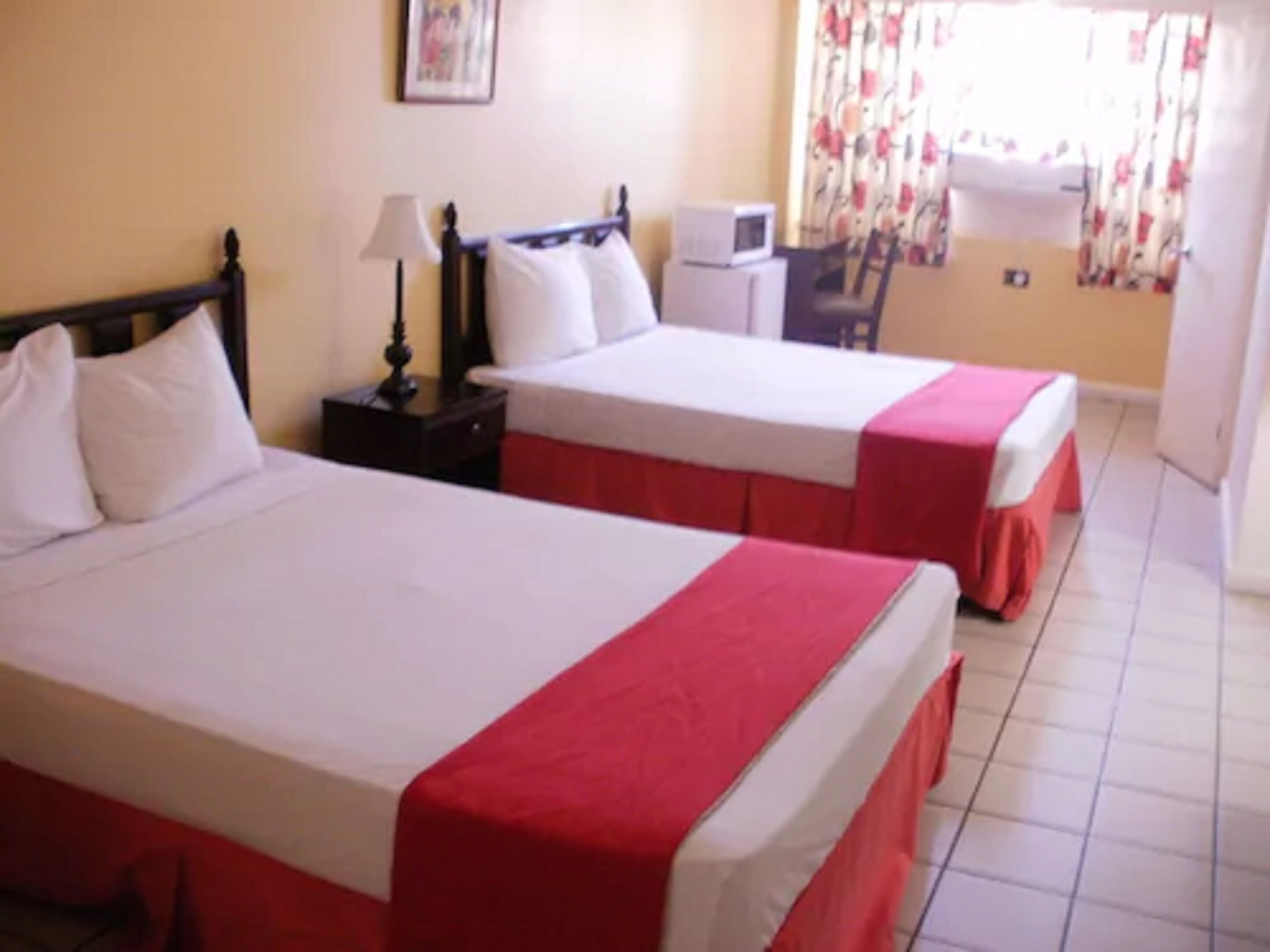 A hotel room with two beds, a desk, a chair, a lamp, and a window with curtains.