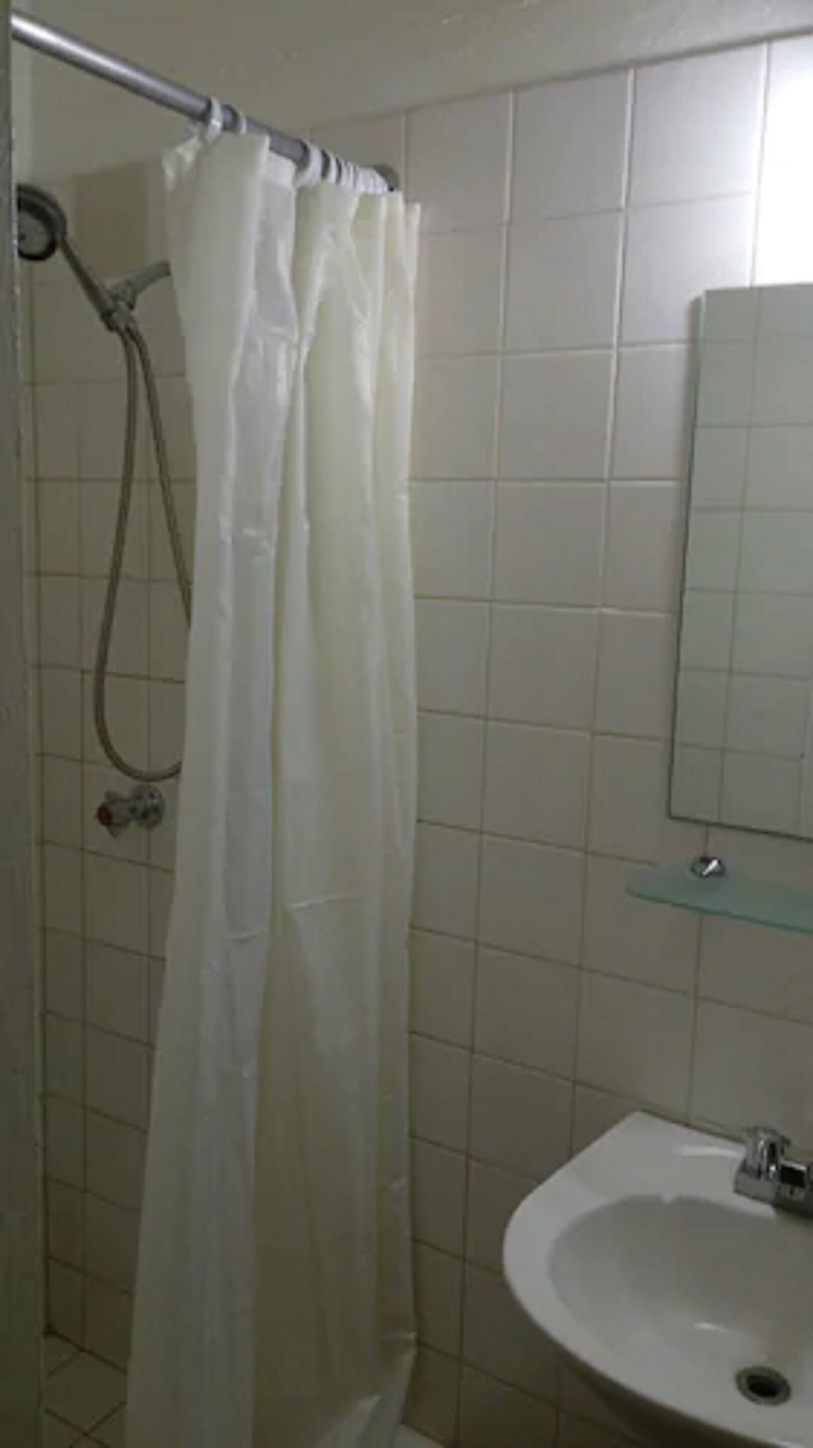 A bathroom with a shower curtain, a glass shelf, and a sink.
