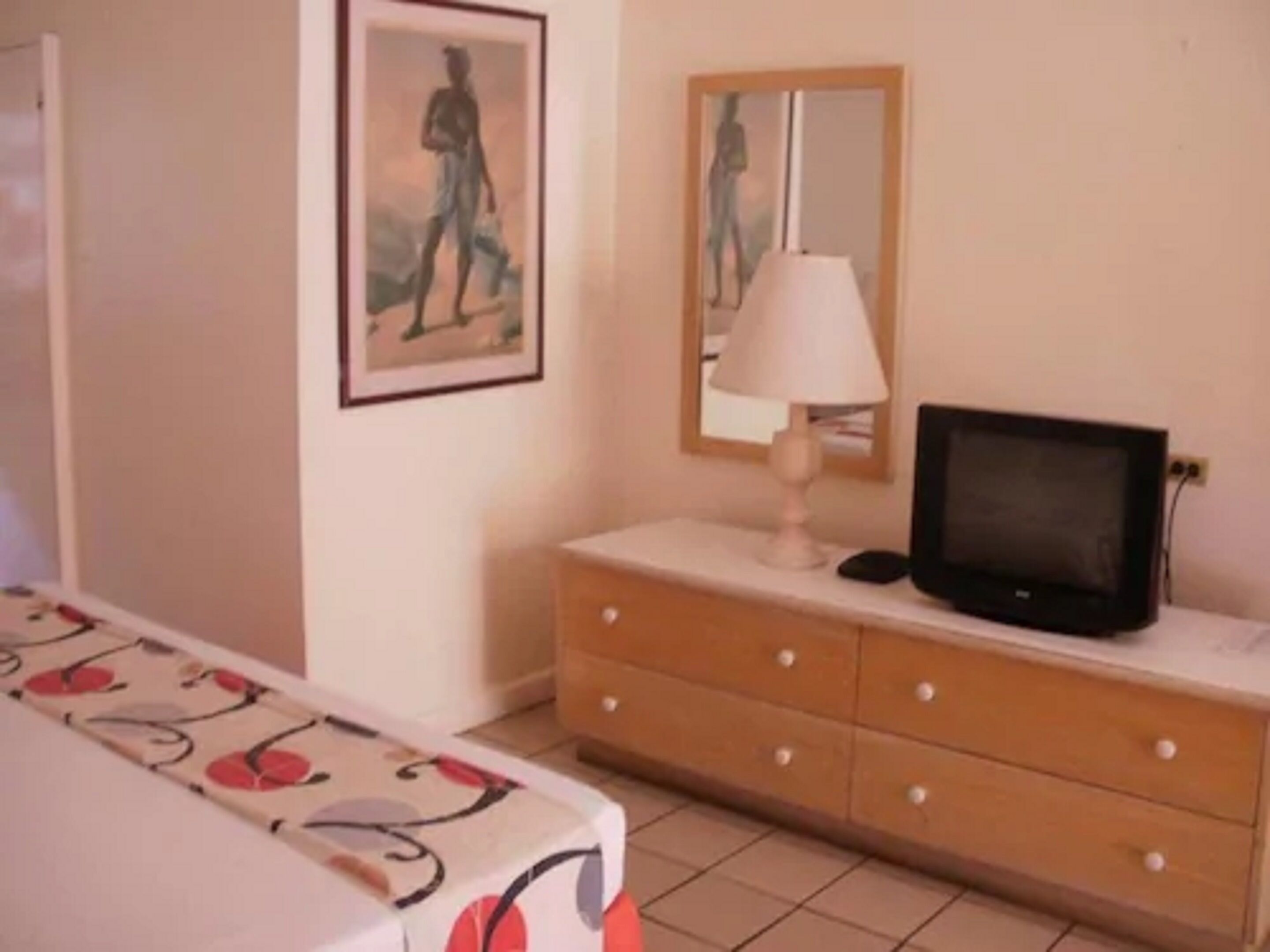 Una habitación con una cama, un tocador con televisor, una lámpara y dos cuadros en la pared.