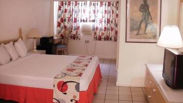 Una habitación de hotel con cama, escritorio, silla, televisor y un cuadro en la pared.