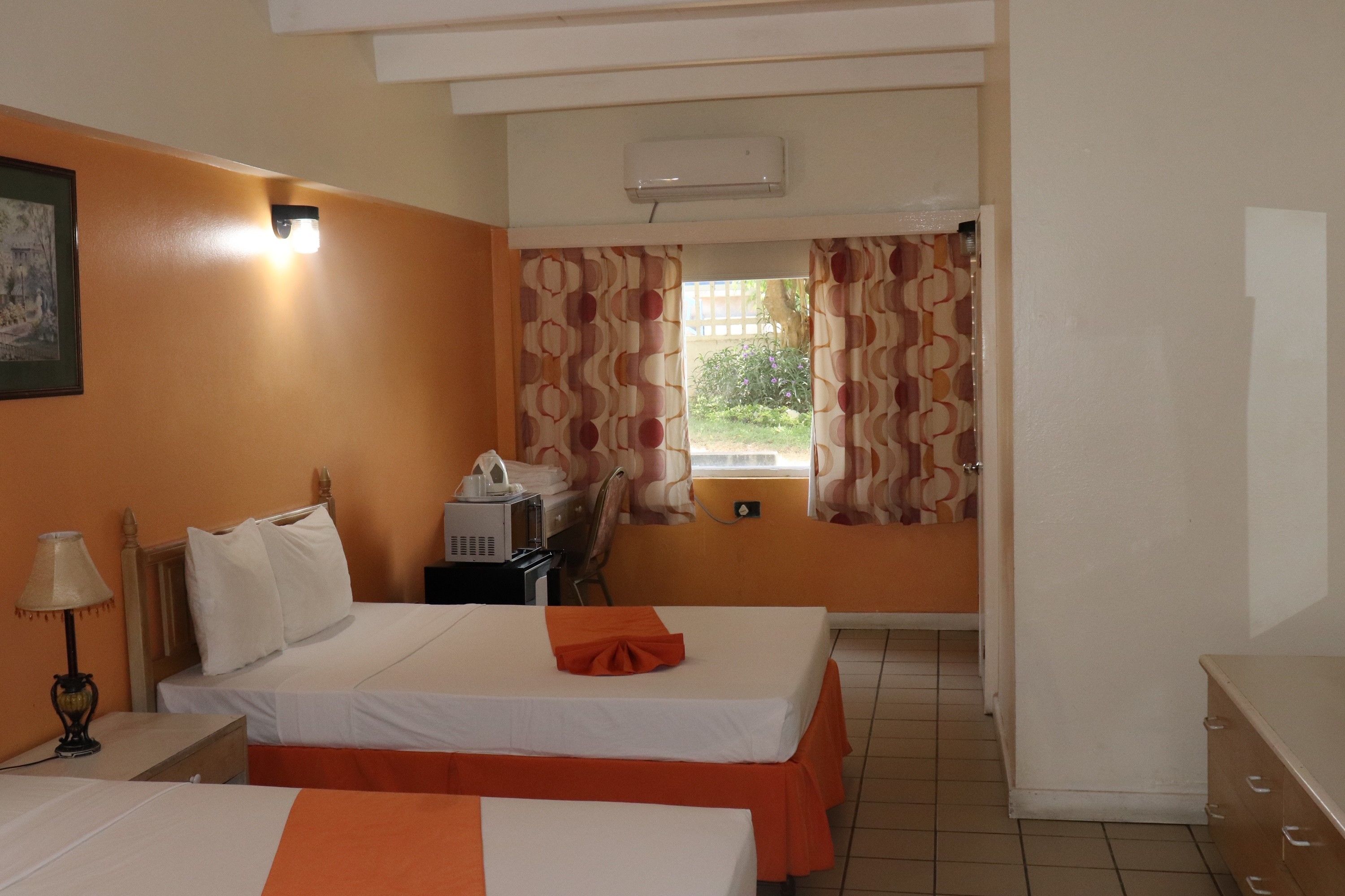 Habitación de hotel con dos camas, un escritorio, una lámpara y una ventana con cortinas.