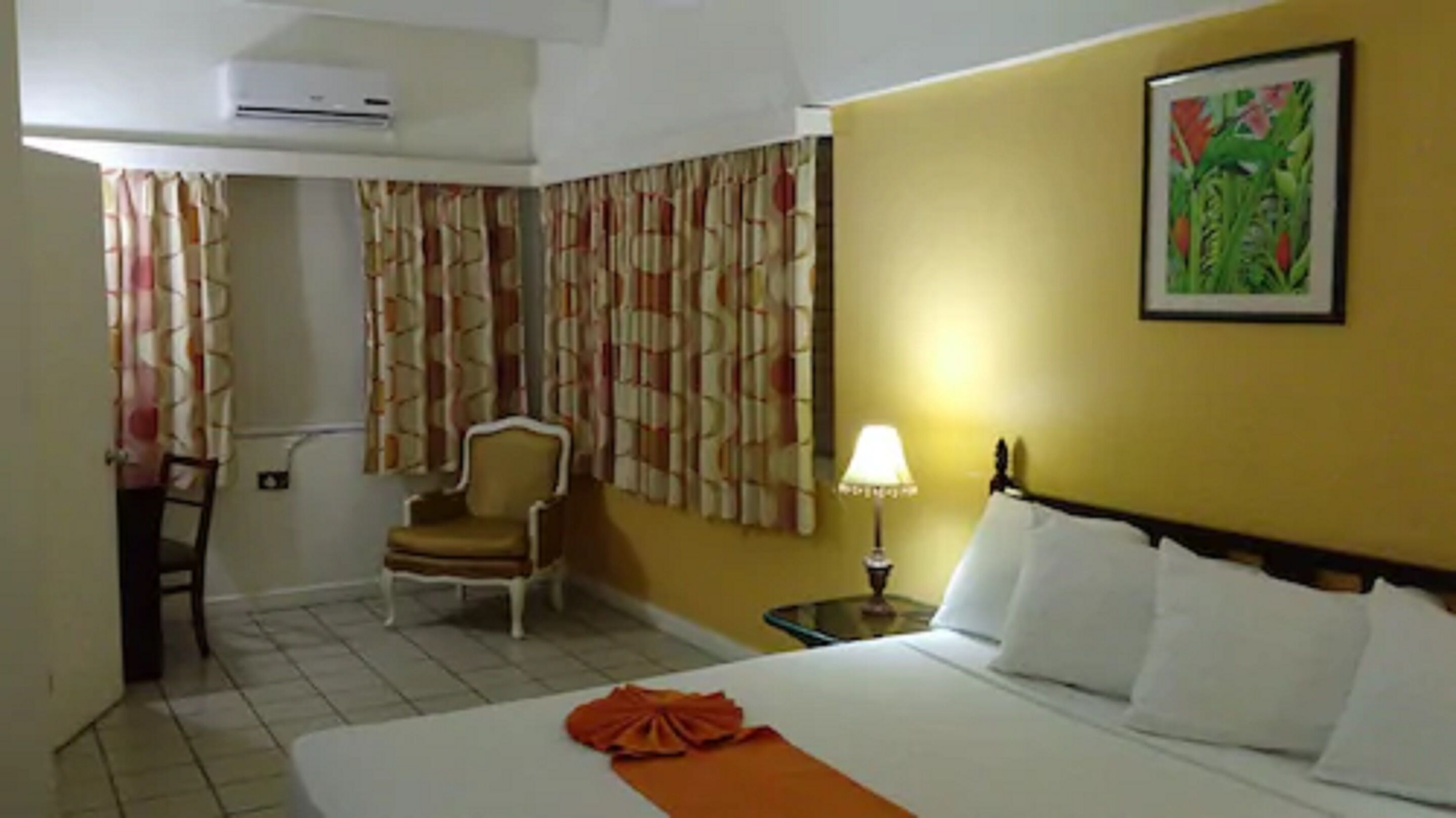 Una habitación de hotel con cama, una silla, una lámpara y cortinas.