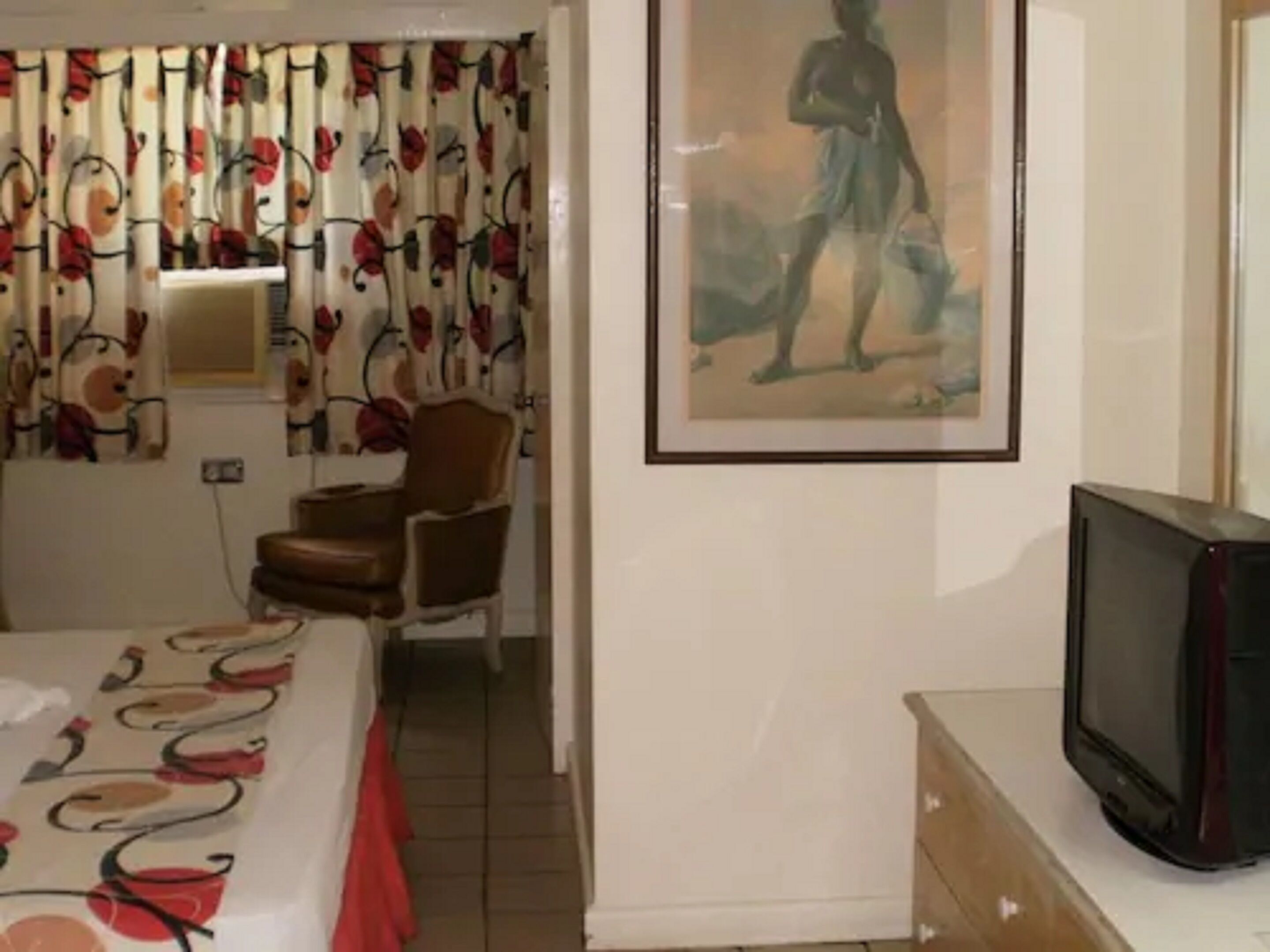 Ett hotellrum med en säng, en stol, en tv och en tavla på väggen.