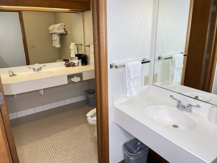 A modern bathroom with a white sink, a mirror, and a toilet. There are towels and toiletries on the sink counter.